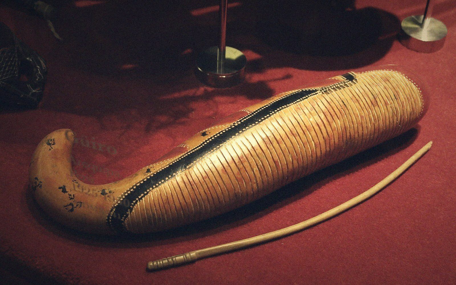 Carved notched gourd instrument displayed with its wooden scraper stick on red fabric