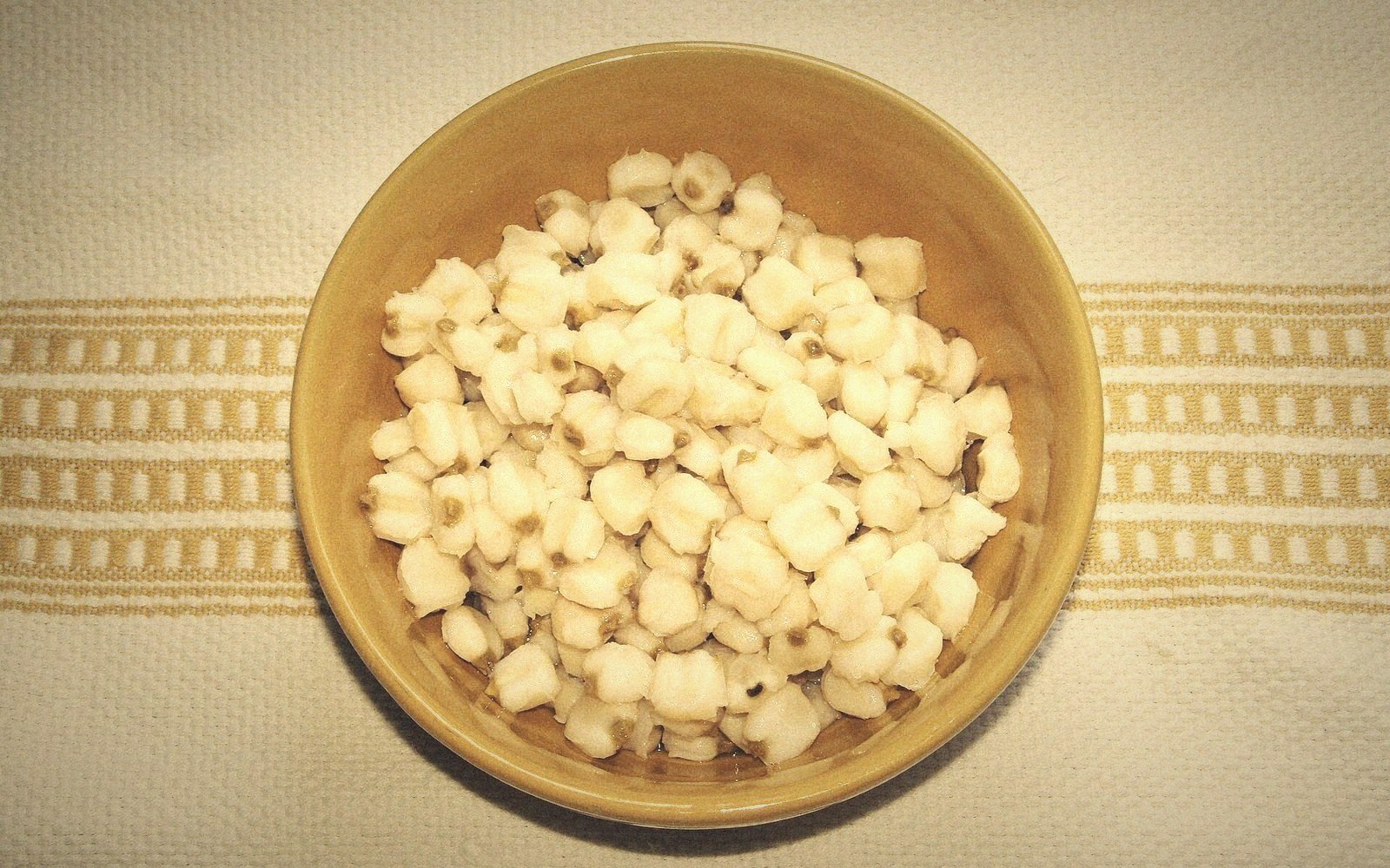A brown bowl filled with white hominy kernels on a striped cloth