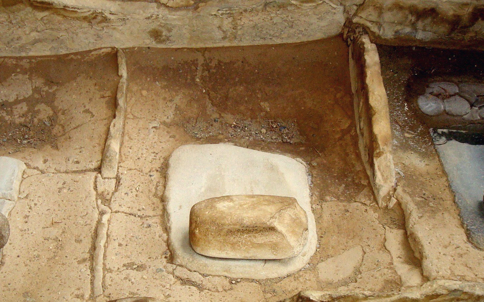 A stone grinding slab and mano set into a partially excavated earthen floor